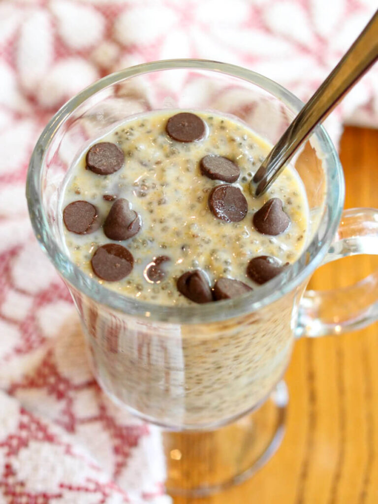 A glass with high protein chia seed pudding with a spoon in it on a wood table.