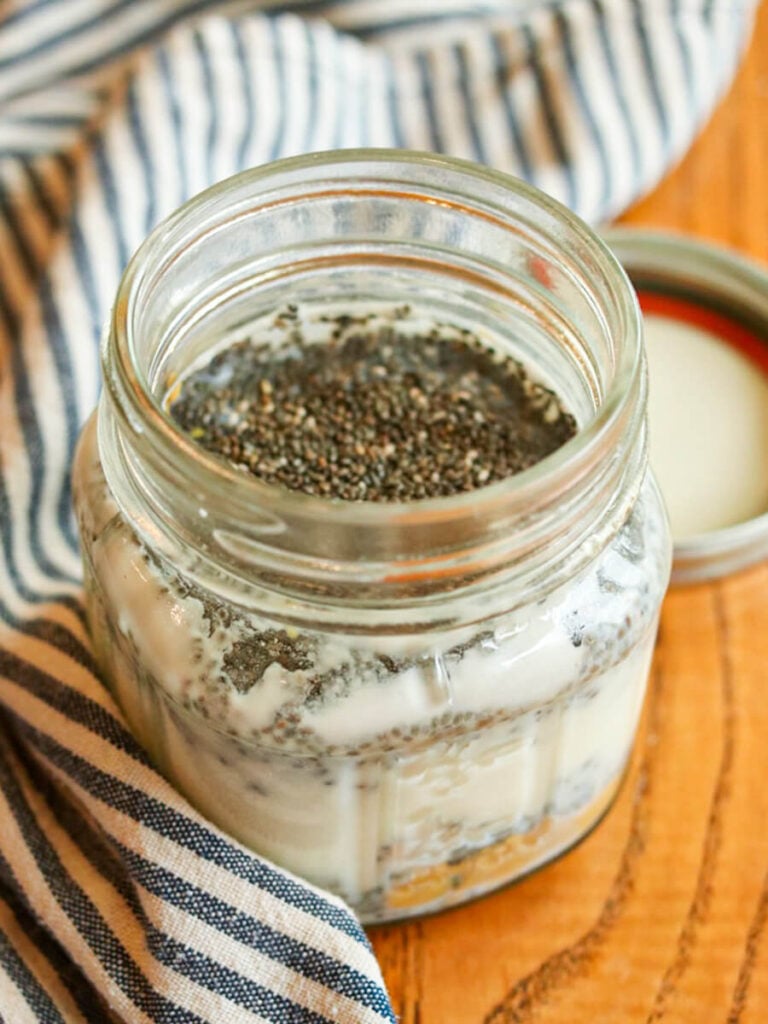 Chia seeds, milk, and other ingredients in a mason jar on a wood table.