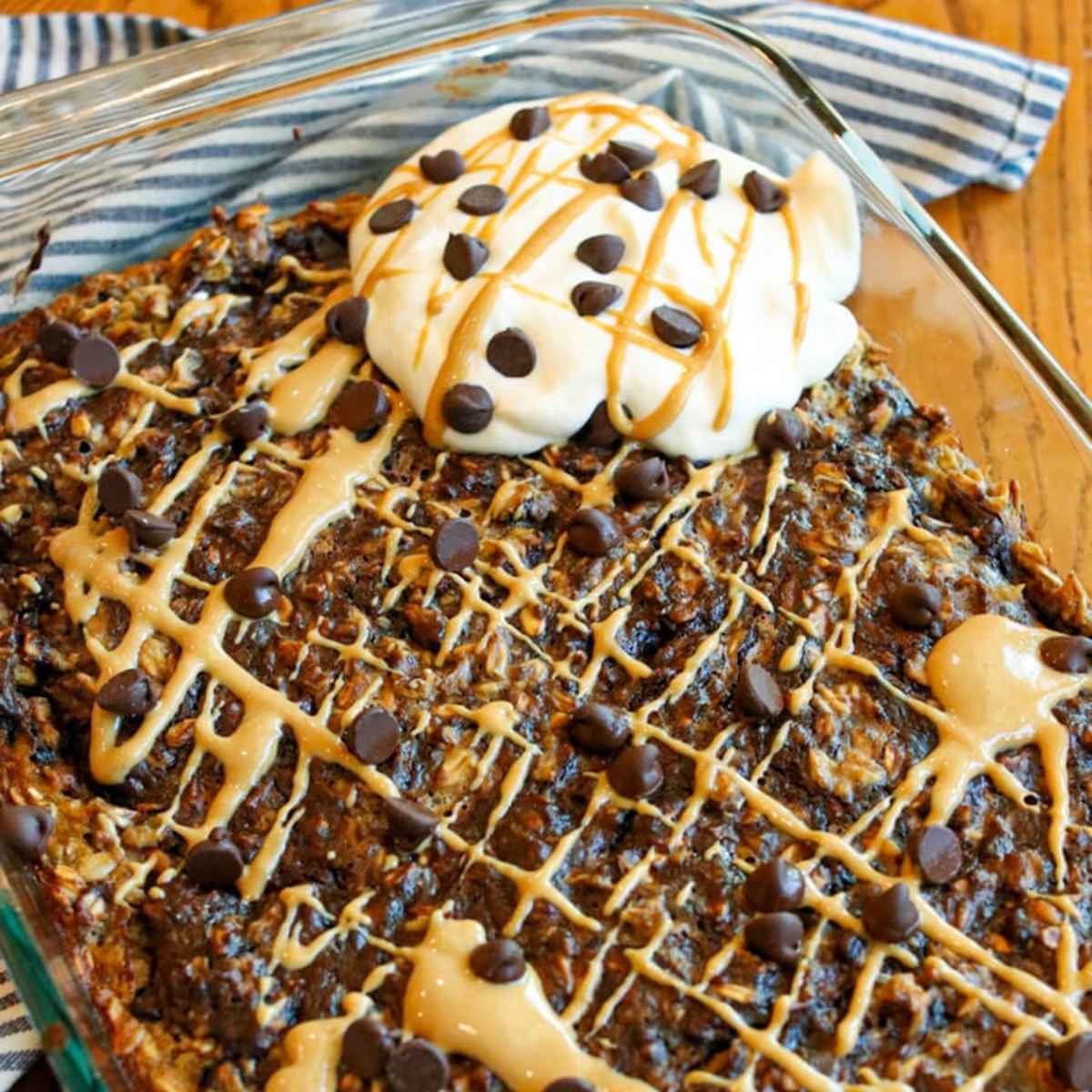Close-up view of chocolate baked oatmeal in a baking dish topped with peanut butter, chocolate chips, and whipped cream.