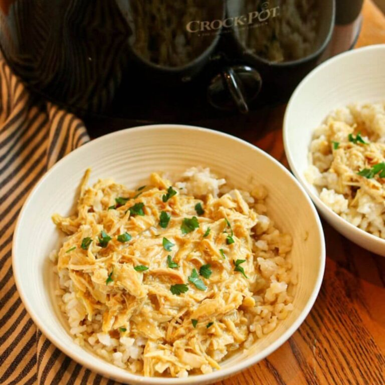 Close up of crockpot honey mustard chicken in a bowl with rice and parsley on a wooden table.