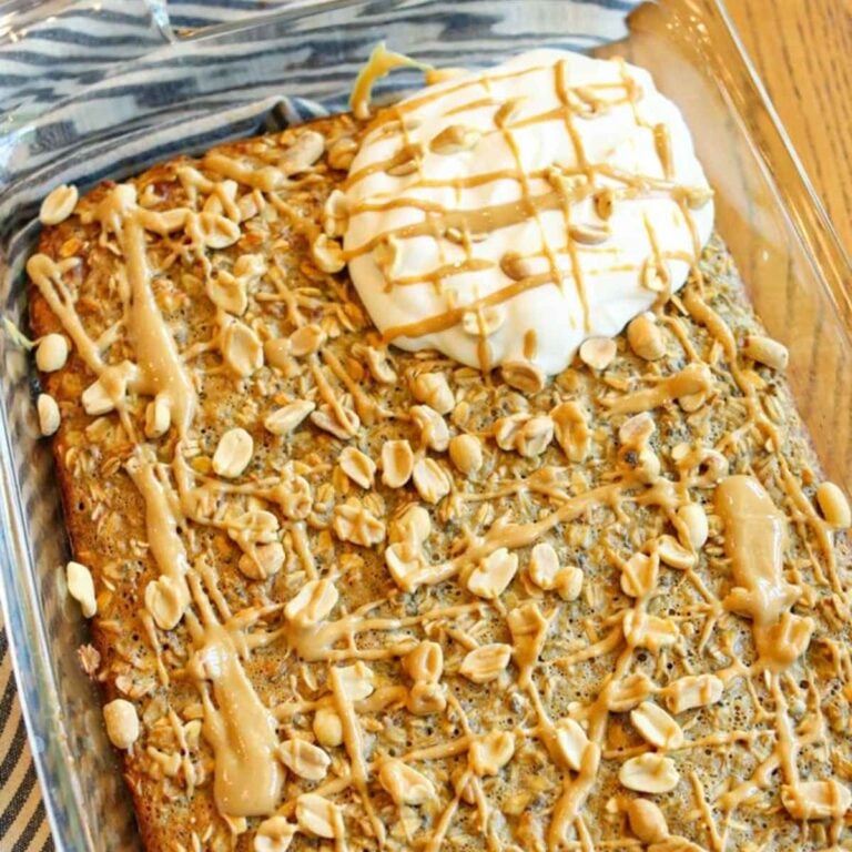 Close-up view of peanut butter baked oatmeal in a baking dish topped with peanut butter, roasted peanuts, and whipped cream.