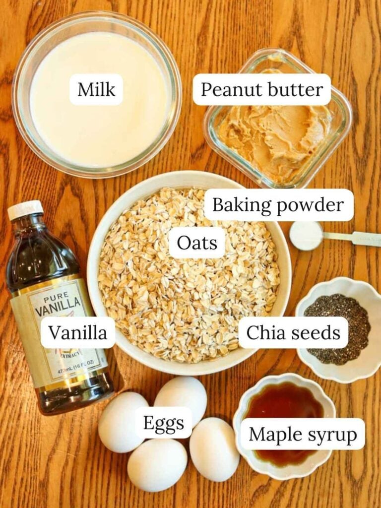 Labeled ingredients o a wood table including oats, milk, peanut butter, maple syrup, vanilla, eggs, chia seeds, and baking powder.
