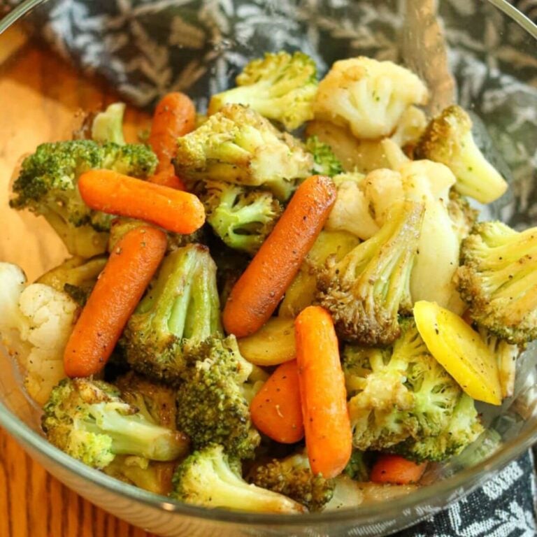 Closeup view of a glass bowl filled with roasted mixed vegetables including carrots, broccoli, and cauliflower.