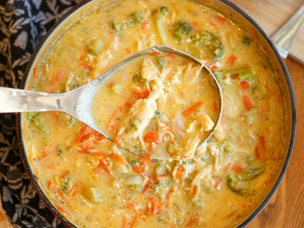 A ladle scooping chicken, broccoli & cheese soup out of a pot.
