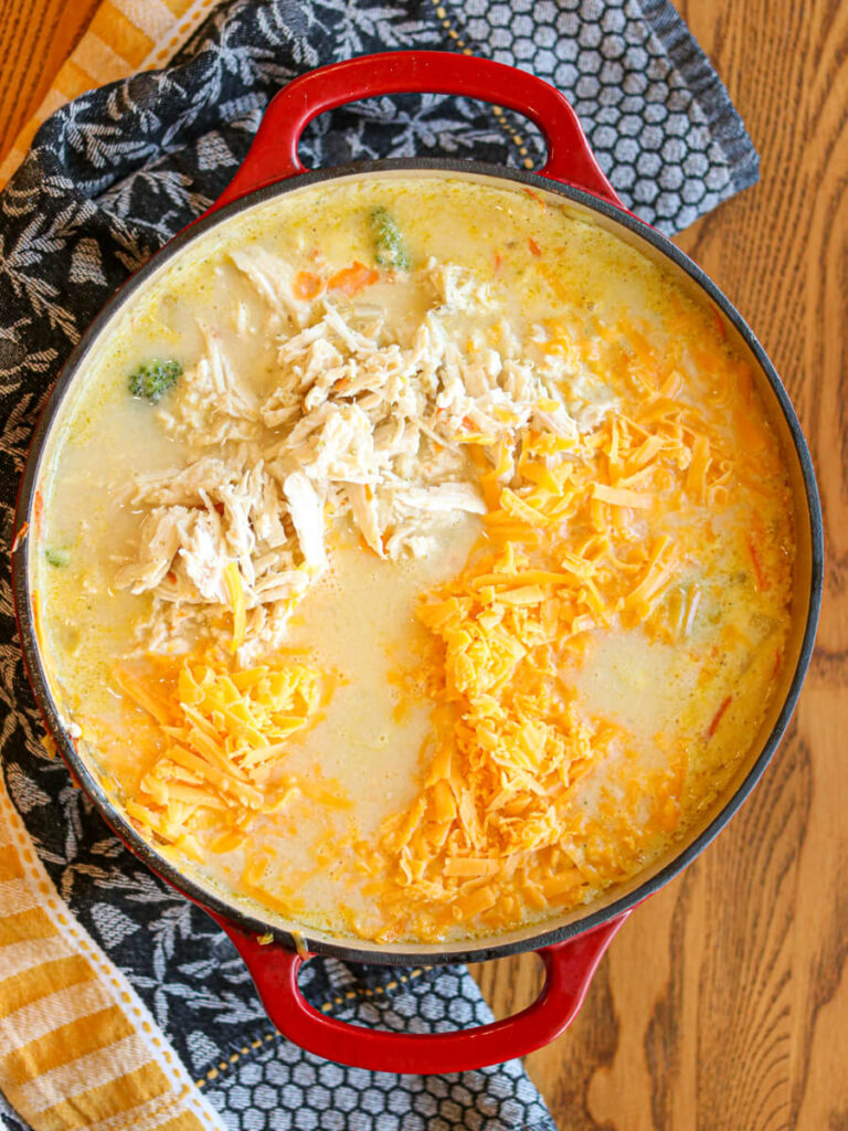 Shredded chicken and shredded cheese being added to a pot of soup.