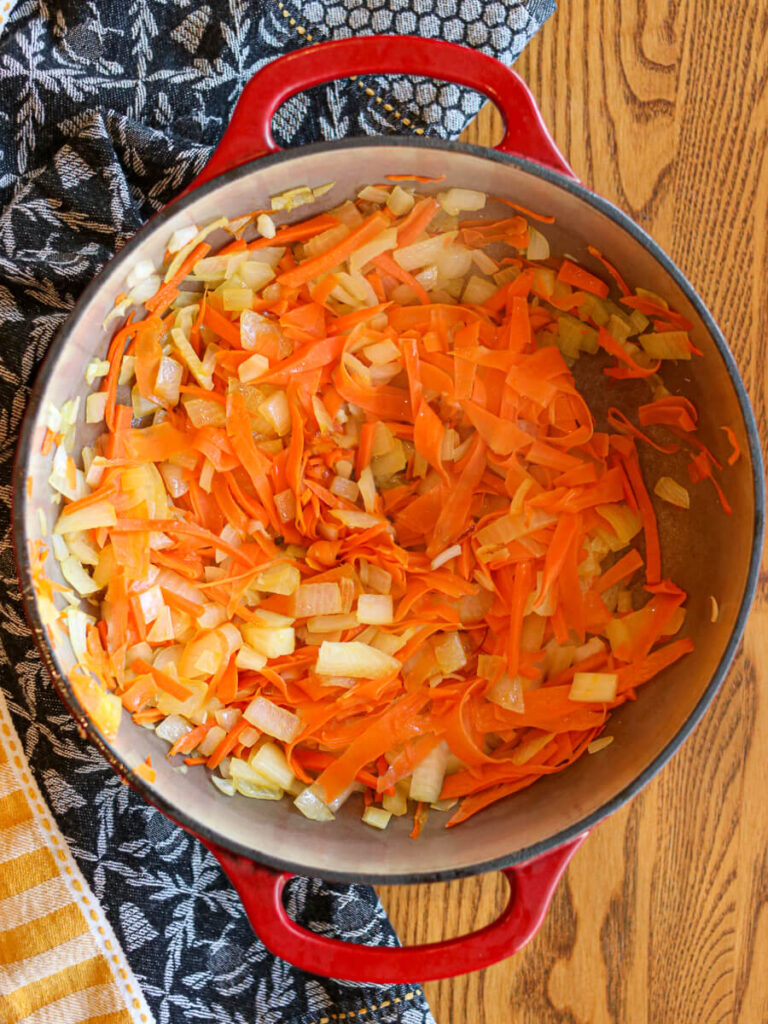 Onions and julienned carrots sautéing in a dutch oven.