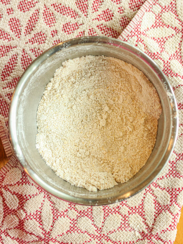 Oat flour and other dry ingredients in a mixing bowl on a kitchen towel.