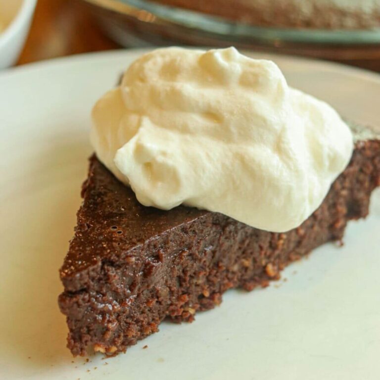 Closeup view of a slice of gluten-free fudge pie topped with whipped cream on a plate.
