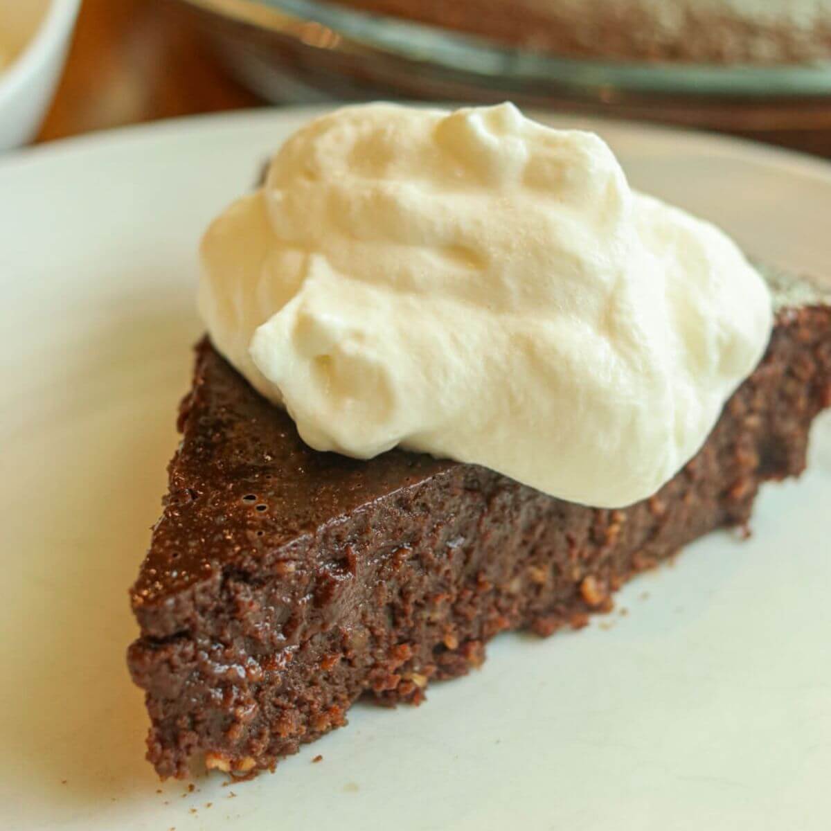 Closeup view of a slice of gluten-free fudge pie topped with whipped cream on a plate.