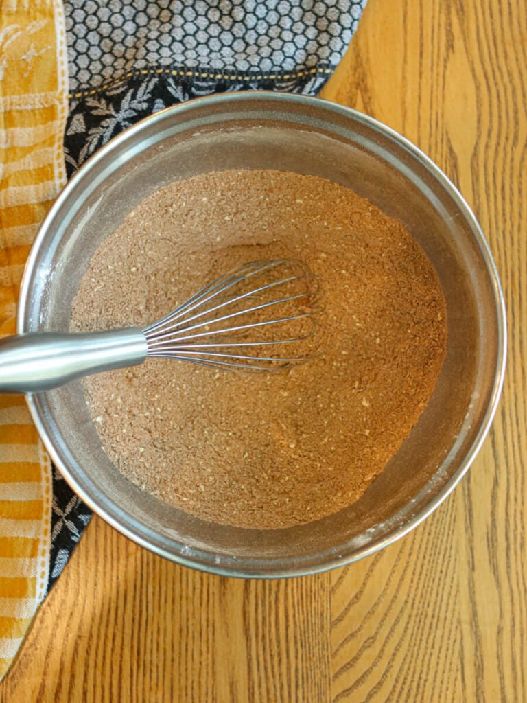Mixing bowl with dry ingredients with a whisk in it on a wood table.