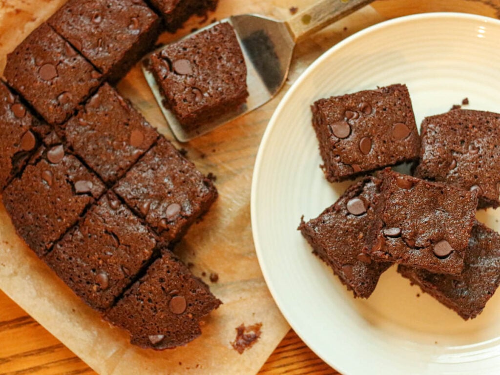 Sliced brownies on parchment paper and stacked on a plate.