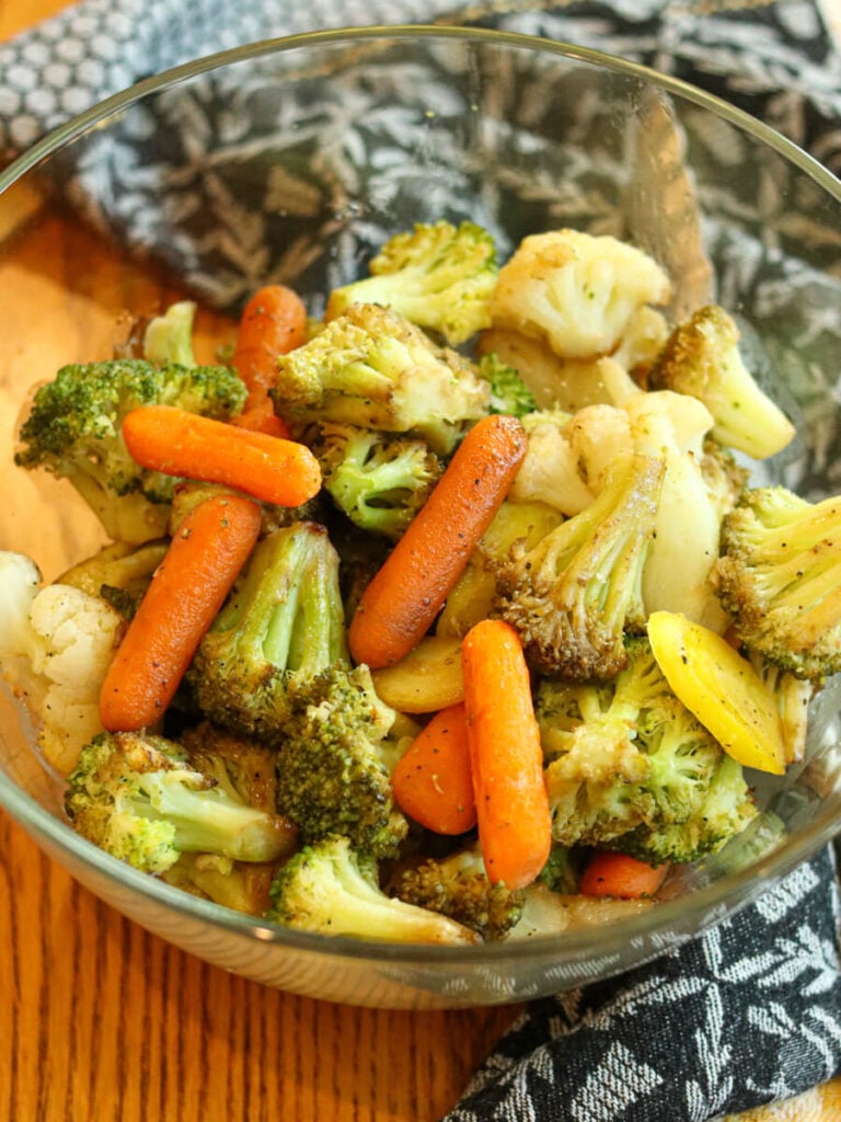 Close view of roasted frozen vegetables in a glass bowl on a table.