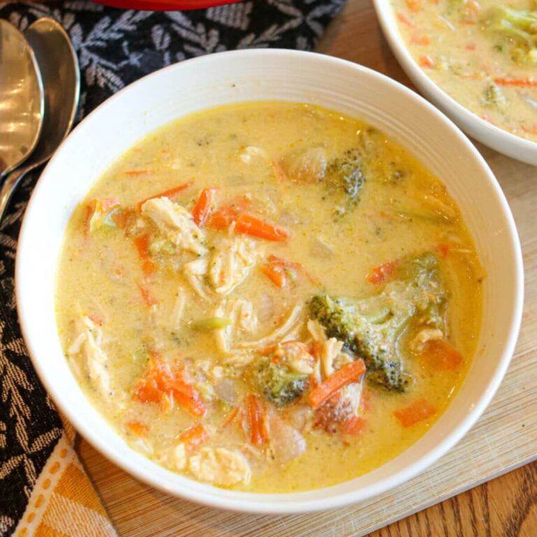 Closeup view of a bowl of chicken, broccoli, and cheese soup on a wood surface.